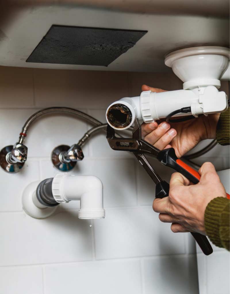 Plumber using pliers to disassemble a bathroom sink drain pipe clogged with buildup for drain cleaning 