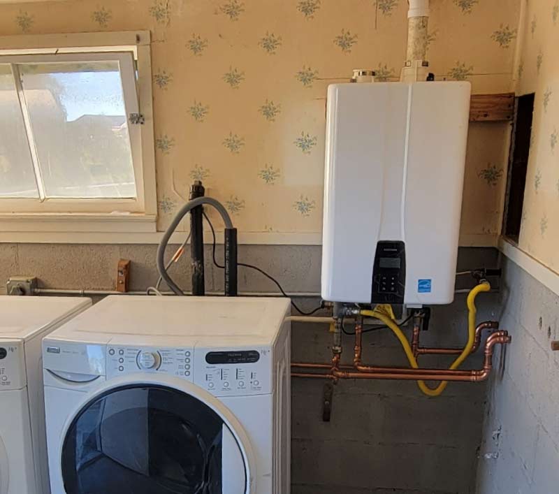 Tankless water heater installed in a home laundry room with copper and gas line connections