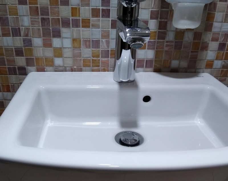 Close-up of a bathroom sink drain with chrome faucet and mosaic tile backsplash