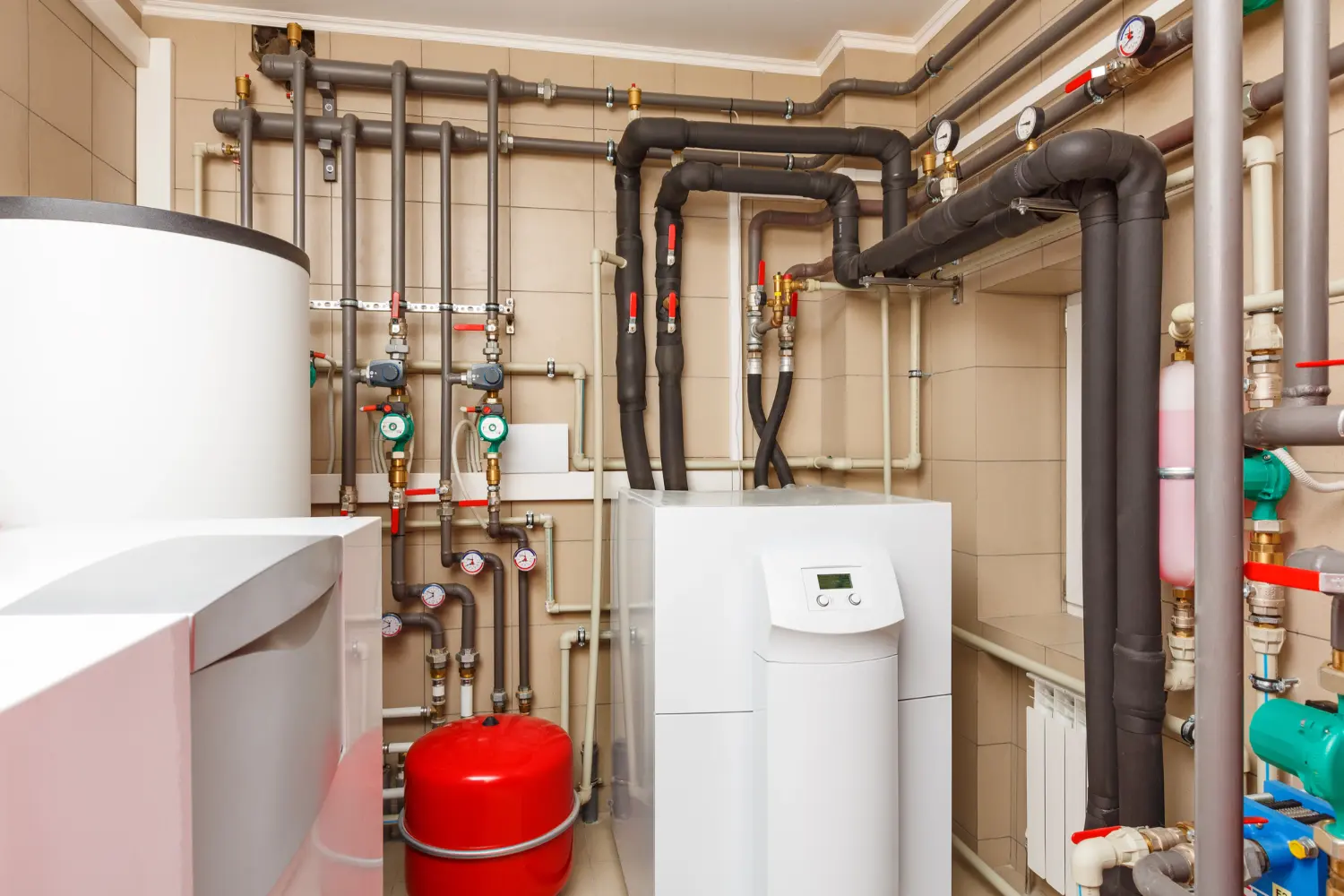 Tankless water heater and storage tank system with red and blue expansion tanks and copper piping in a mechanical room after water heater repair